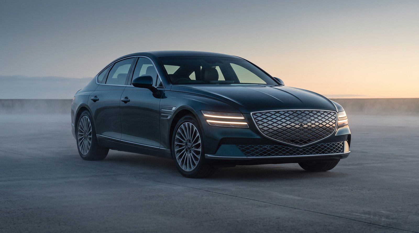 The AURION X parked on an empty concrete plateau at dawn, the first pale light of sunrise on the horizon behind it
